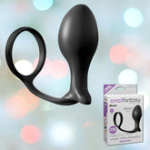 A black Anal Fantasy Collection Ass Gasm Cock Ring with an anal plug from Pipedream on a blurred multicolored background. The plug features a large bulbous shape and a narrowing tip, crafted for incredible prostate stimulation. In the lower right corner, the "Anal Fantasy Collection" box displays the same product inside.